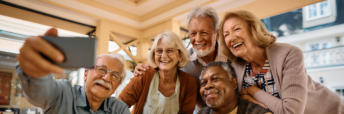 Multiracial group of happy senior people taking selfie with cell phone in nursing home.